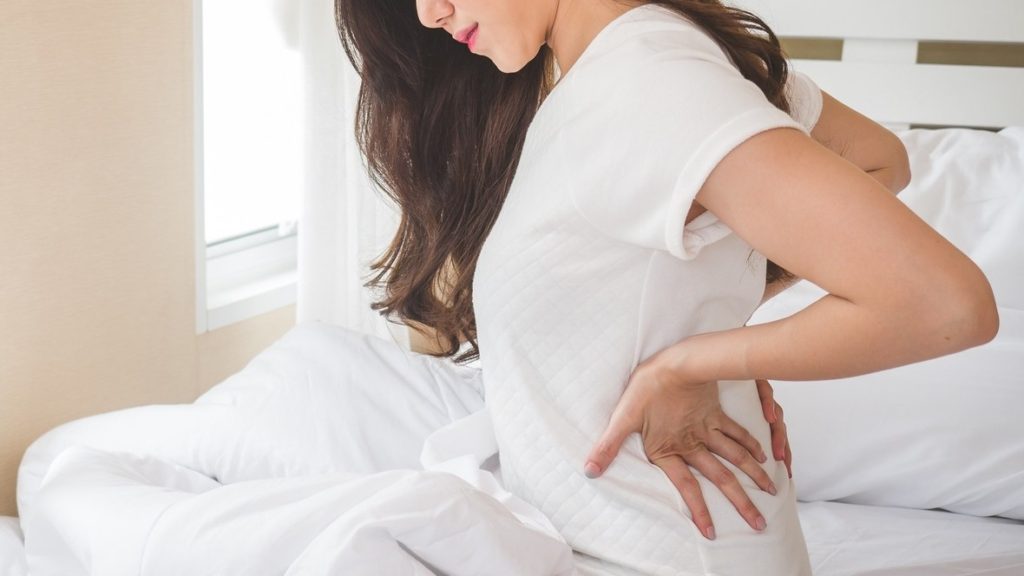 Woman sitting on bed with hands on her back